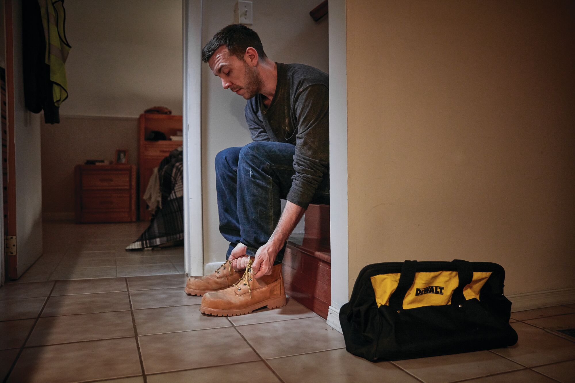 Image of man lacing up boots while sitting down with DeWalt contractor bag next to him
